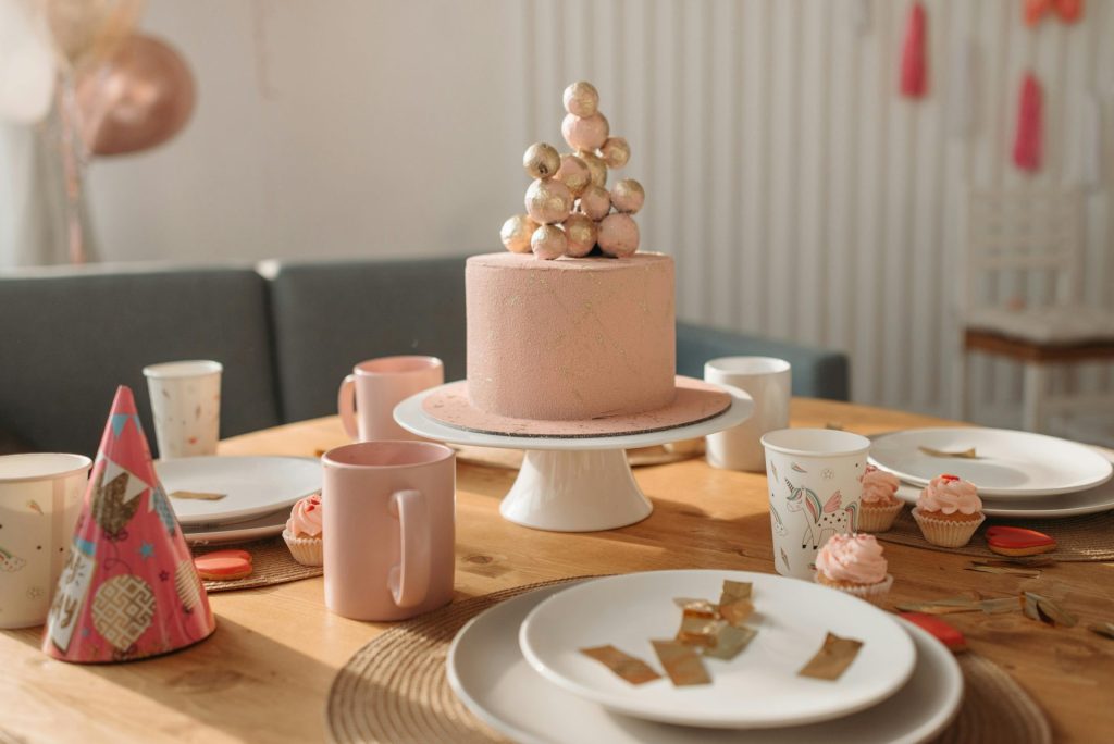 Pink birthday cake with decorations on a dining table set for a festive party indoors.